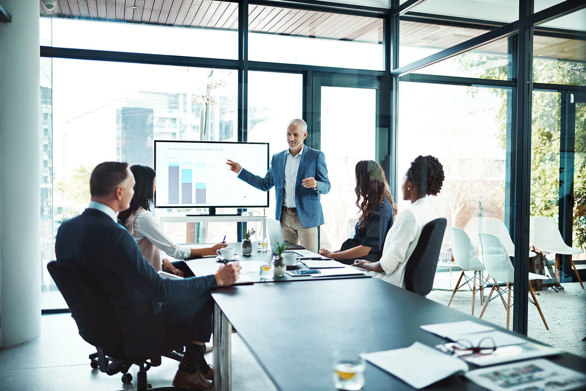 securus-consulting-banner A man in front of a large screen presenting to a table full of people