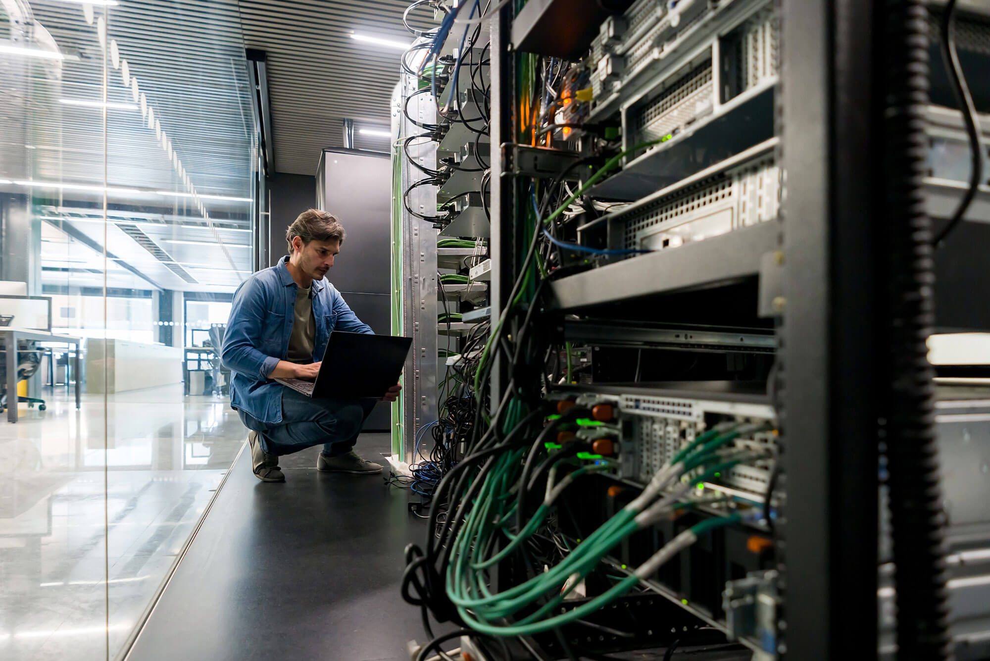A crouching man along a bank of servers. Data backup and recovery.