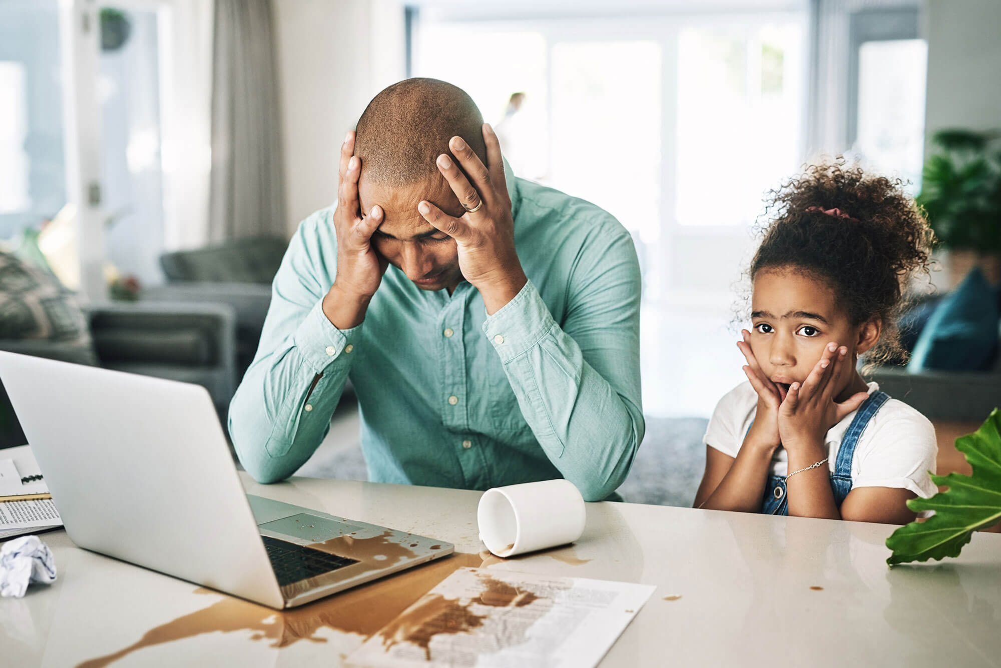 A man at a laptop with his head in his hands. His daughter has spilled his coffee all over the keyboard. data backup and recovery